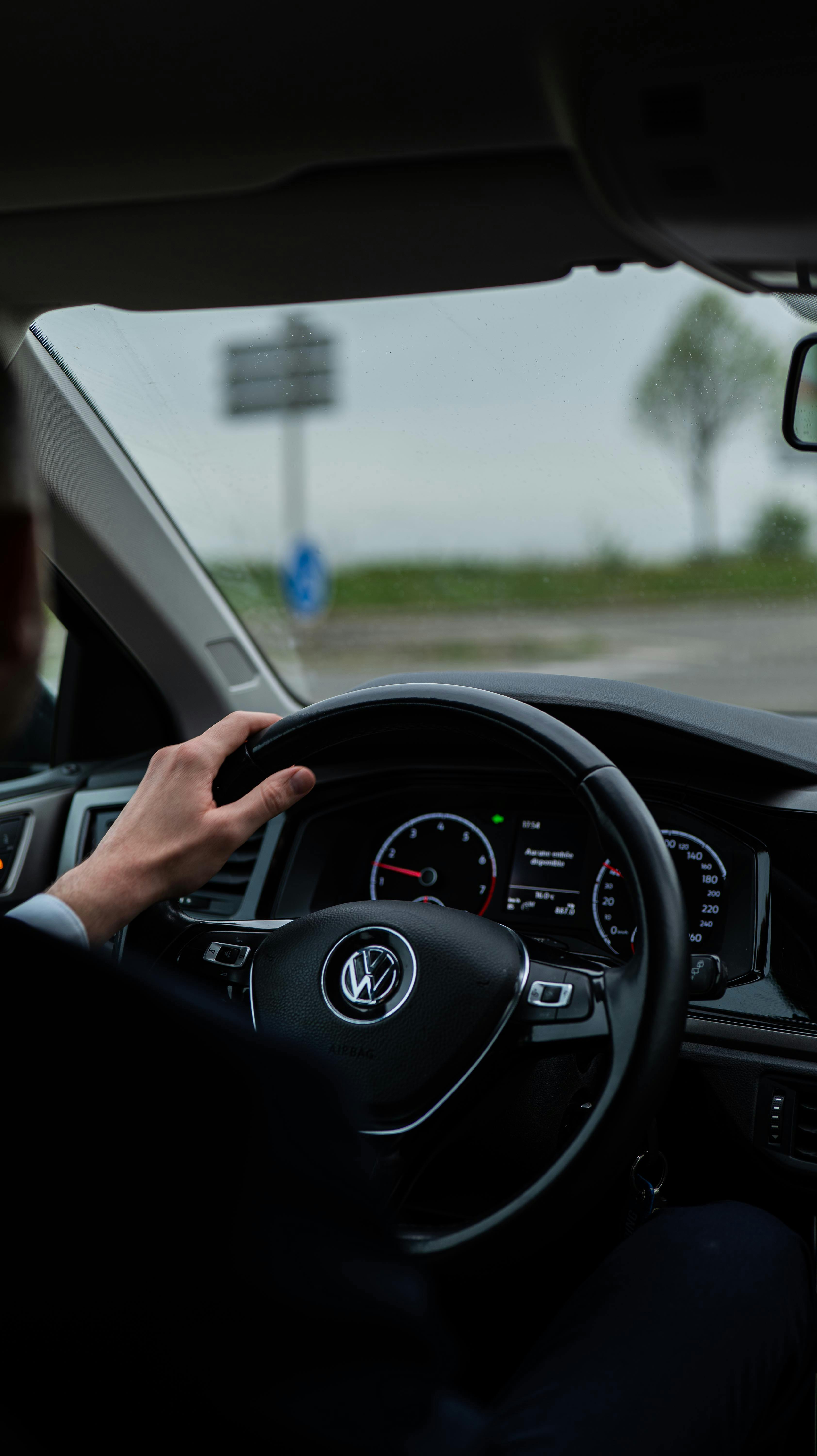 View from driver's seat showing car dashboard and steering wheel. Outdoors scene.
